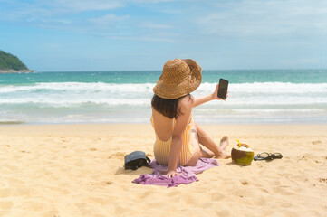 Wall Mural - Young Beautiful woman in Bikini listening to music and using smartphone on the beach,  Summer, vacation, holidays, Lifestyles concept.