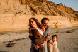 © Erin Brant/Stocksy - Joyful family hugging mom on beach