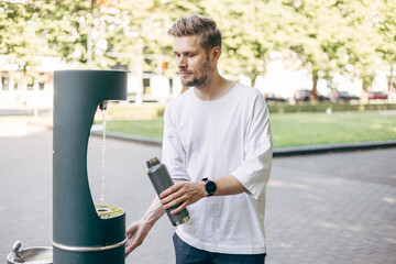 Man refilling his water bottle at the city. Free public water bottle refill station. Sustainable and green city. Heat wave. Tap water to reduce plastic bottle usage. Drinking water dispenser