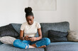 © Ezequiel Giménez/Stocksy - African American teenager browsing social media on sofa