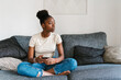 © Ezequiel Giménez/Stocksy - Black young female with smartphone relaxing on couch