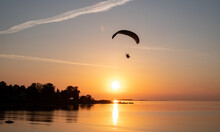 Paraglider Pilot Flies In The Sky During Sunset On Beautiful Beach. Paraplane Silhouette. Adventure Vacation And Travel Concept.