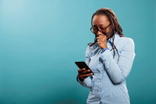 Upset Young Woman Crying After Reading Tragic News On Smartphone Device While Standing On Blue Background. Sad Unhappy Adult Person In Tears While Reading Unfortunate Message.