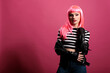 Confident punk woman wearing rocker leather jacket in studio, expressing carefree funky fashion style. Attractive beautiful lady with trendy clothes and stylish pink hair, cute makeup.