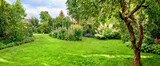 A magical and lush green garden with various colorful flowers blooming and trees growing in spring or summer. Beautiful cultivated botanical garden landscape with bright sunshine on a picturesque day