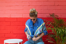 Young Woman Wearing A Retro Jacket Sitting In Front Of A Colorful Wall