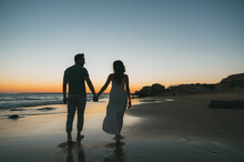 Loving Couple Holding Hands On Beach At Sunset