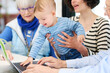 © Guille Faingold/Stocksy - Baby playing with laptop with his family around.