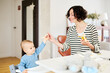© Guille Faingold/Stocksy - Mother feeding baby with banana at lunchtime.