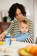 © Guille Faingold/Stocksy - Mother with baby sitting at table.