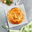 Classic turkish pie with meat on wooden board. Composition with burek pie on concrete background with textile and spices. Balkan pie with minced meat  in rustic style on gray table.