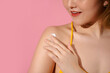© Marc Tran/Stocksy - Beautiful woman applying cream on shoulders, isolated on pink