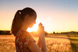 © kieferpix - Young woman meditating, praying with her eyes closed, practicing self awareness with hands in prayer position against a beautiful sunset.