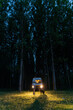© Alba Vitta/Stocksy - Man and dog in camper van at night with lights on in the woods
