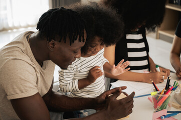 The family of African father and  Asian mother playing wood puzzles with their two daughters in the living room. To enhance the development of the youngest child. Concept of getting ready for school