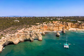 Aerial photo on arco natural in Lagoa. View of Praia da Marinha. In the background, there are cliffs, the beach and the coast. Catamaran in the ocean. Lagoa, Algarve, Portugal