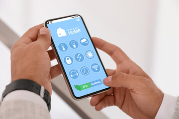 Man using Smart Home app on mobile phone indoors, closeup