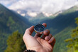 © yanik88 - A hand with a compass against the backdrop of epic snow-capped mountains with clouds and a forest at the foot, close-up