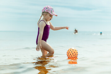 cute little girl playing with rubber ball in sea