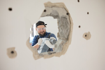 Poster - Demolition of an old house. Demolition of unnecessary walls with hand-held impact hammer. A view of an experienced construction worker trying with all his might to enlarge hole in wall.