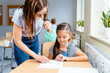 © Iryna - Teacher helping cute little girl with writing lesson at classroom.