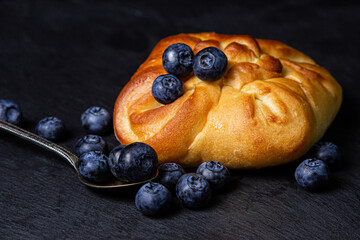 Wall Mural - Bun with blueberries on a black background. Fresh homemade cakes. Berry dessert