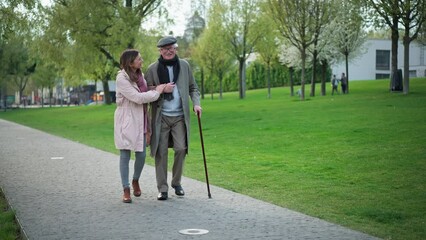 Wall Mural - Happy senior man with walking stick and adult daughter outdoors on a walk in park.