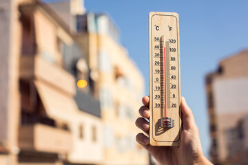 Fototapete - Hot weather. Thermometer in front of an urban scene during heatwave.