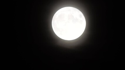 Wall Mural - Glowing huge full moon as seen from earth through the clouds against starry night sky. Large full moon moves across the sky, moon makes its way from bottom left frame to top right.