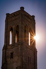 Canvas Print - Vertical shot of old stone architecture tower with sunlight under blue sky