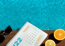 Top View Of Swimming Pool With Orange, Lemon, Sunglass And Calendar On The Wooden Floor. Summer Vibes. Summer Calendar. Summer August. August Month. Summer Calendar 2022. Summer Time