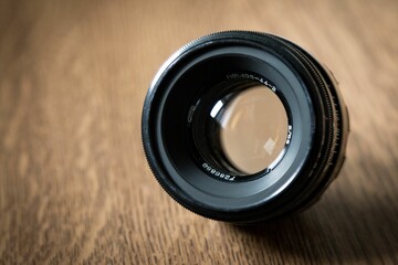 Sticker - Closeup shot of a camera lens placed on a brown wooden table