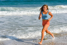 Pretty athletic young woman in shorts and crop top running on the sunny beach