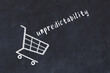 Chalk drawing of shopping cart and word unpredictability on black chalboard. Concept of globalization and mass consuming
