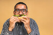 © denis_vermenko - Hungry young african american black man eating hamburger isolated over beige background. Diet or Fast food concept.