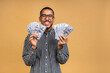 © denis_vermenko - Happy winner! Young rich african american man in casual t-shirt holding money dollar bills with surprise isolated over beige wall.