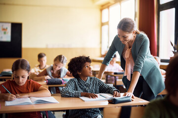 Black schoolboy talks to his teacher during class in classroom.