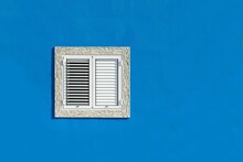 Small Window With Closed White Shutters On Blue Wall