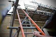 Low Angle Shot Of Human Hand On Ladder And Scaffold Leaning On Brick Building For Roof Renovation