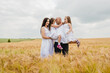 © sharshonm - The concept of a friendly family.Mom, dad and daughters hug in a wheat field.Cute beautiful children.Family vacation.Happy family resting in summer park.Cheerful children picnicking in the park.
