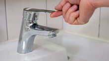 Strong Male Hand Opens Water Faucet. Water Stream Flows From Tap. Clear Water Runs Quickly And Man Forgets To Turn Off Water Closeup