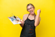 Young Artist Caucasian Woman Holding A Palette Isolated  On Yellow Background Celebrating A Victory