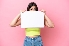 Young Brazilian Woman Isolated On Pink Background Holding An Empty Placard And Hiding Behind It