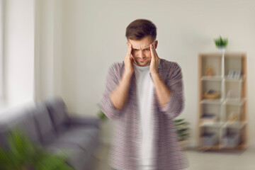 Young man feeling dizzy. Man standing in living room, feeling pain and spinning vertigo sensation in his head. Headache, health problems, BPPV, brain tumor concept