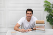 © Vitaliy - Portrait of young handsome student sitting at the desk with a stack of books. Education and preparation for exams concept