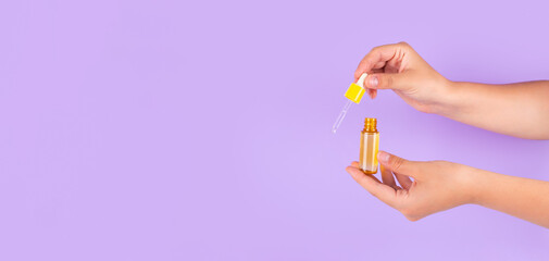 Beautiful groomed woman's hands with yellow serum with vitamin c on purple background. Nourishing oil for clean and soft skin. Healthcare concept