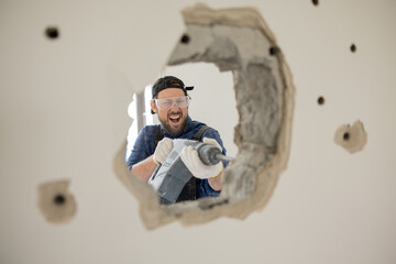 Wall Mural - Crazy energetic man vandalizes apartment with impact hammer forges wall punches a hole through concrete, house construction site.