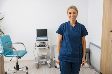 Wall Mural - Smiling doctor, ultrasound specialist looking at camera on her workplace in clinic