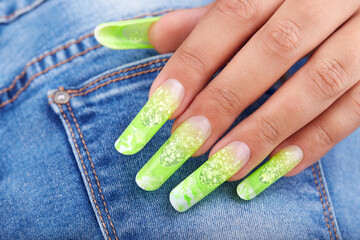 Wall Mural - Hand with long artificial French manicured nails colored with green neon and white on jeans denim textile background