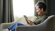 Leinwandbild Motiv Happy middle aged woman relaxing on couch, using tablet computer, reading news from internet. Senior woman studying online. Profile of middle aged woman in chair with tablet on day light background